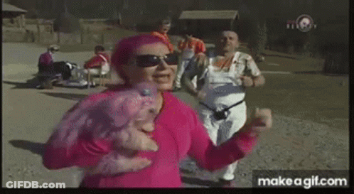A Woman In A Pink Shirt Is Dancing In A Park With Other People . GIF