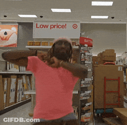 A Woman In A Pink Shirt Is Dancing In Front Of A Sign That Says Low Price GIF
