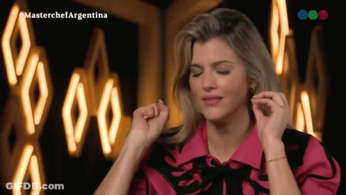 A Woman In A Pink Shirt Is Dancing In Front Of A Sign That Says Masterchefargentina GIF