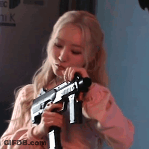A Woman In A Pink Shirt Is Holding A Gun . GIF