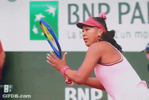A Woman In A Pink Shirt Is Holding A Tennis Racquet In Front Of A Bnp Pa Sign GIF