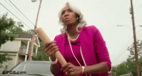 A Woman In A Pink Shirt Is Holding A Wooden Rolling Pin In Her Hands . GIF