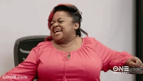 A Woman In A Pink Shirt Is Laughing While Sitting At A Table . GIF