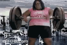 A Woman In A Pink Shirt Is Lifting A Barbell In A Gym GIF