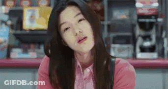 A Woman In A Pink Shirt Is Sitting At A Counter In A Store And Making A Funny Face . GIF