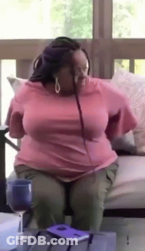 A Woman In A Pink Shirt Is Sitting On A Couch With Her Legs Crossed . GIF