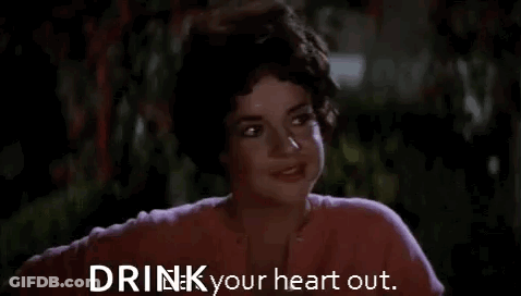 A Woman In A Pink Shirt Is Smiling And Says `` Drink Your Heart Out . '' GIF