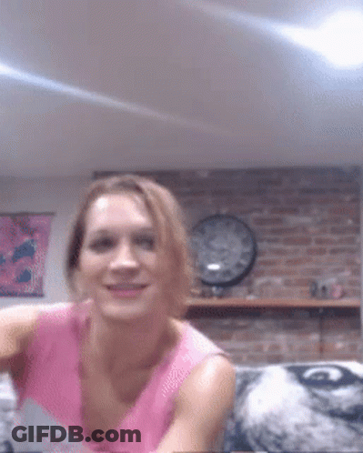 A Woman In A Pink Shirt Is Smiling In Front Of A Brick Wall And A Clock GIF
