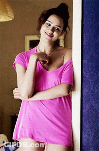 A Woman In A Pink Shirt Is Standing In Front Of A Blue Wall GIF