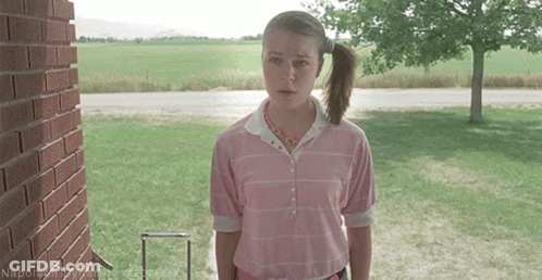 A Woman In A Pink Shirt Is Standing In Front Of A Brick Building GIF