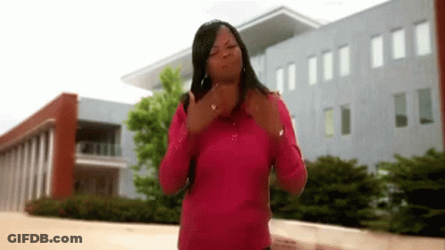 A Woman In A Pink Shirt Is Standing In Front Of A Building And Giving The Middle Finger . GIF