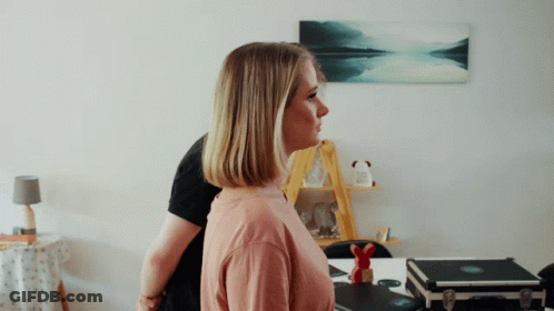 A Woman In A Pink Shirt Is Standing In Front Of A Man In A Black Shirt GIF