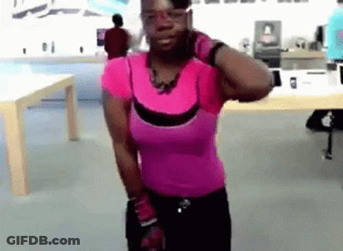 A Woman In A Pink Shirt Is Standing In Front Of A Table GIF