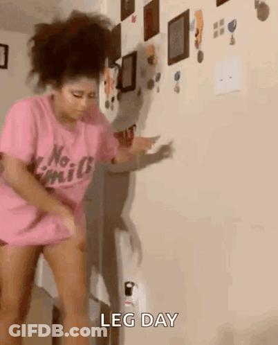 A Woman In A Pink Shirt Is Standing In Front Of A Wall And Dancing . GIF