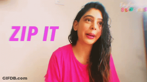 A Woman In A Pink Shirt Is Standing In Front Of A Wall That Says Zip It GIF