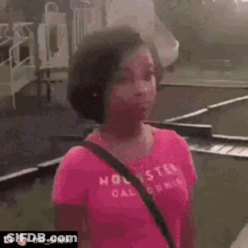 A Woman In A Pink Shirt Is Standing On A Sidewalk With A Bicycle In The Background And Says Do You Wanna Fight ? GIF