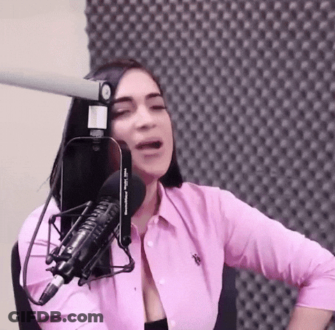 A Woman In A Pink Shirt Is Talking Into A Microphone GIF
