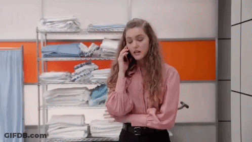 A Woman In A Pink Shirt Is Talking On A Cell Phone In Front Of A Shelf Of Towels . GIF