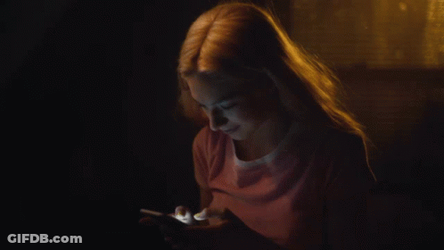 A Woman In A Pink Shirt Is Using A Cell Phone In The Dark GIF