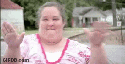 A Woman In A Pink Shirt Is Waving Her Hands In The Air . GIF