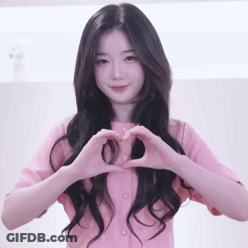 A Woman In A Pink Shirt Making A Heart Shape With Her Hands GIF