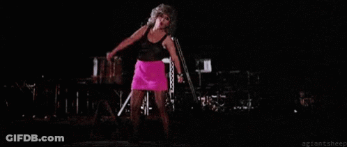 A Woman In A Pink Skirt Is Singing Into A Microphone On Stage . GIF