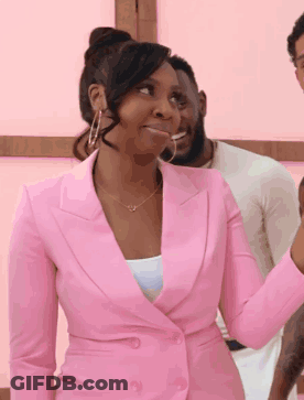 A Woman In A Pink Suit And Hoop Earrings Is Standing In Front Of A Man . GIF