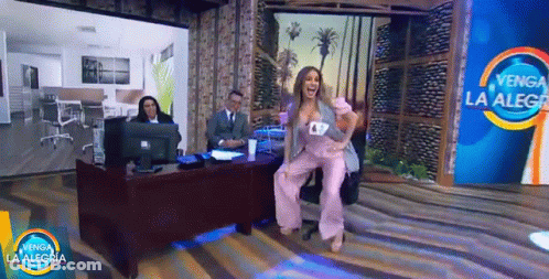 A Woman In A Pink Suit Is Dancing In Front Of A Sign That Says " Venga La Alegria " GIF