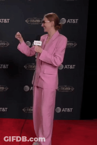 A Woman In A Pink Suit Is Holding A Microphone In Front Of An At & T Wall GIF