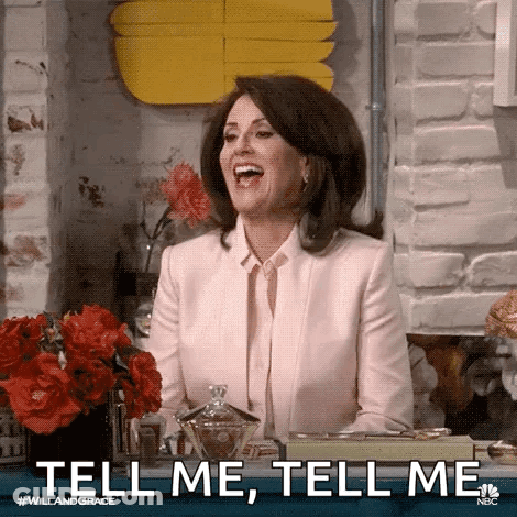 A Woman In A Pink Suit Is Sitting At A Table Laughing And Saying `` Tell Me , Tell Me '' . GIF