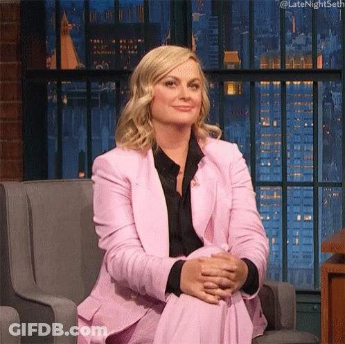 A Woman In A Pink Suit Is Sitting In A Chair With Her Legs Crossed And Her Hands Folded . GIF