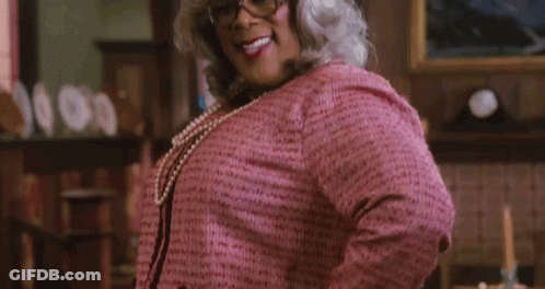 A Woman In A Pink Sweater And Pearls Is Smiling With Her Tongue Out GIF