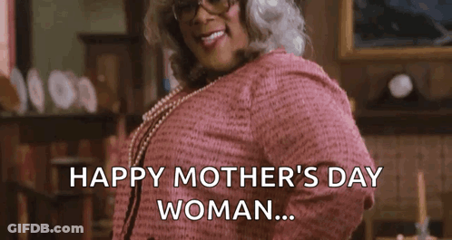 A Woman In A Pink Sweater And Pearls Is Standing In A Living Room . GIF