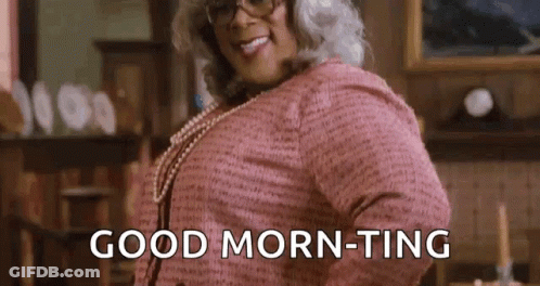 A Woman In A Pink Sweater And Pearls Is Standing In A Living Room And Saying `` Good Morning '' . GIF