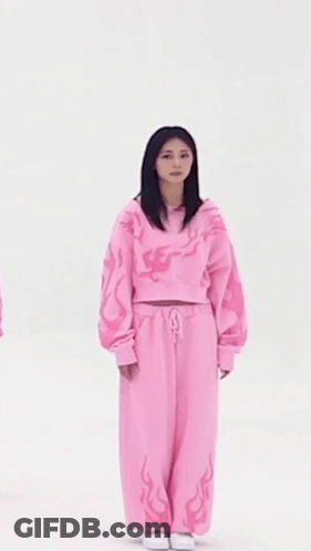 A Woman In A Pink Sweater And Pink Sweatpants Is Standing In Front Of A White Background . GIF