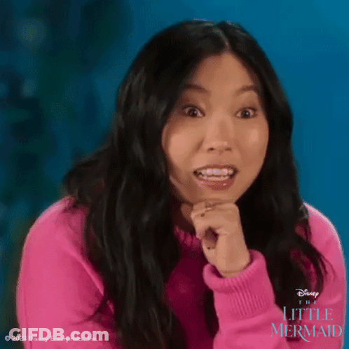 A Woman In A Pink Sweater Is Making A Surprised Face While Holding Her Hands To Her Chin . GIF