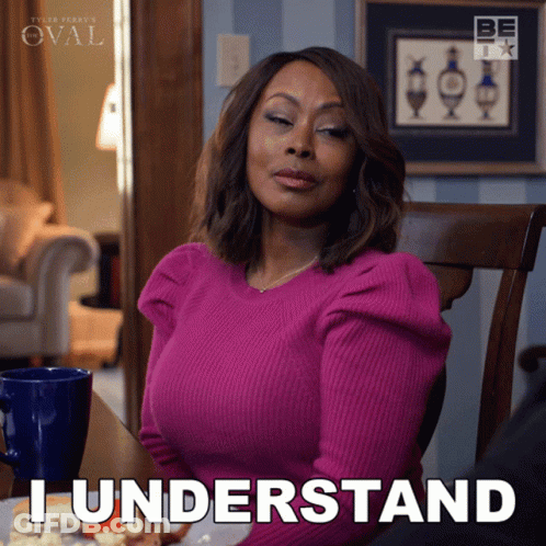 A Woman In A Pink Sweater Is Sitting At A Table And Says " I Understand " GIF