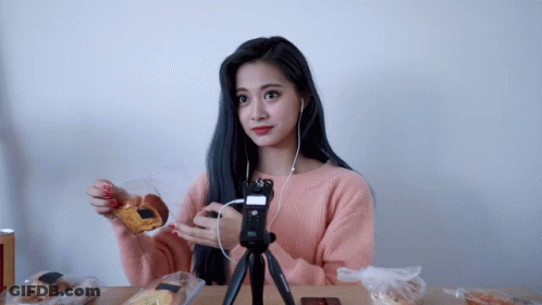 A Woman In A Pink Sweater Is Sitting At A Table Eating Food GIF