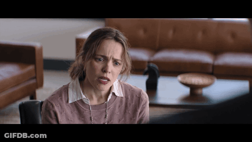 A Woman In A Pink Sweater Is Sitting In Front Of A Couch GIF