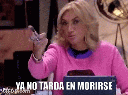 A Woman In A Pink Sweater Is Sitting In Front Of A Laptop And Holding A Cell Phone In Her Hand . GIF