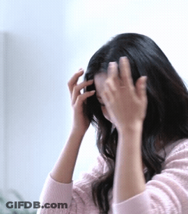 A Woman In A Pink Sweater Is Touching Her Hair With Her Hands GIF