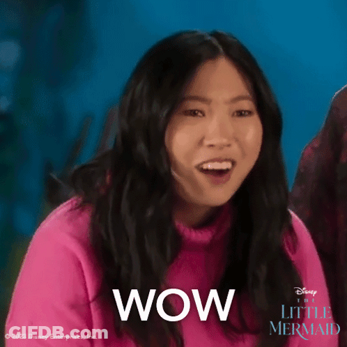 A Woman In A Pink Sweater Says Wow In Front Of A Blue Background . GIF