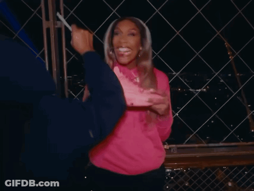 A Woman In A Pink Sweatshirt Holds A Pink Nike Shoe In Her Hand GIF