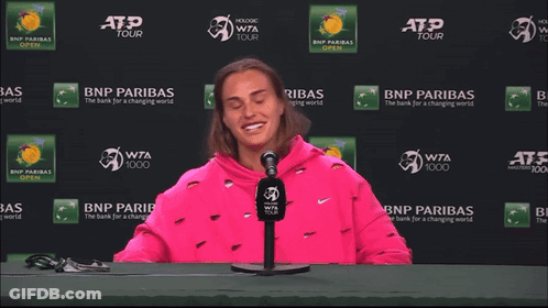 A Woman In A Pink Sweatshirt Is Sitting In Front Of A Bnp Paribas Sign GIF