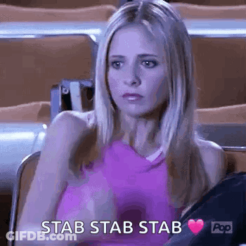 A Woman In A Pink Tank Top Is Sitting In A Stadium With A Heart In Her Hand And The Words `` Stab Stab Stab '' . GIF