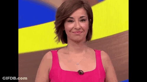 A Woman In A Pink Tank Top Is Smiling While Standing In Front Of A Yellow And Blue Background . GIF