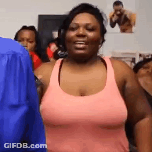 A Woman In A Pink Tank Top Is Standing In Front Of A Group Of People In A Room . GIF