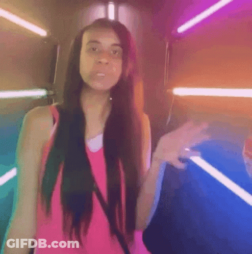 A Woman In A Pink Tank Top Is Standing In Front Of A Neon Sign . GIF