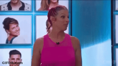 A Woman In A Pink Tank Top Is Standing In Front Of A Wall Of Portraits Of People . GIF