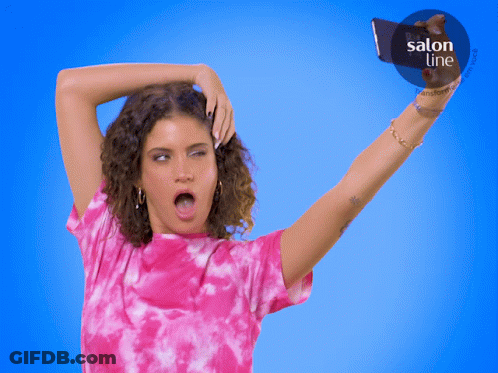 A Woman In A Pink Tie Dye Shirt Takes A Selfie In Front Of A Blue Background That Says Salon Line GIF